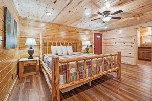 Una habitación tipo cabaña de madera con una cama, dos mesitas de noche, un ventilador de techo y una puerta roja.