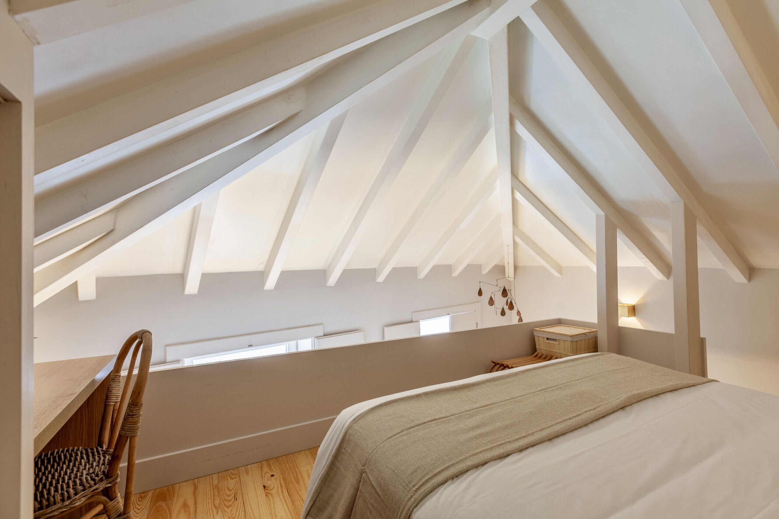 Ein Schlafzimmer mit schrägem Dach, einem Bett, einem Sessel und einem kleinen Nachttisch.