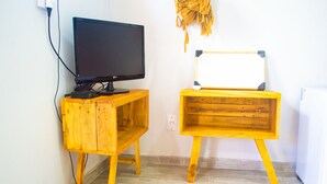 Une pièce comprenant un meuble TV en bois sur lequel est posée une télévision à écran plat, ainsi qu’un bureau en bois doté d’un tableau blanc.