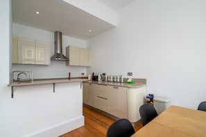 A modern kitchen with a built-in stove, a sink, and a dining area with a table and chairs. - GuestReady - Chic in the heart of Kensington (London)