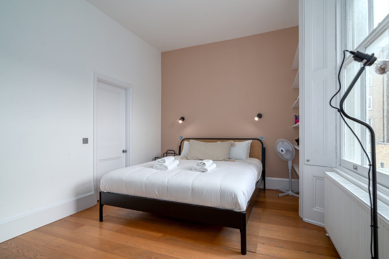 Un dormitorio con cama, una puerta blanca, un radiador y ventana con vista a edificios.