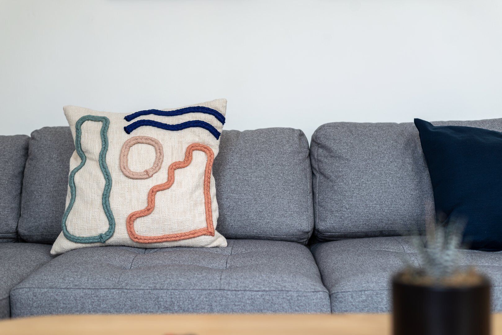 Un canapé gris avec trois coussins : un avec un motif géométrique et deux coussins unis.