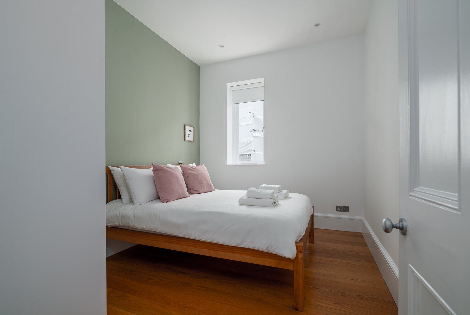 A bedroom with a wooden bed, white bedding, a green wall, a window, and a white door.