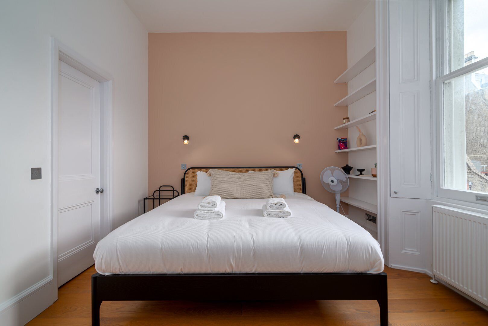 Un dormitorio con cama, mesitas de noche, ventana y radiador.