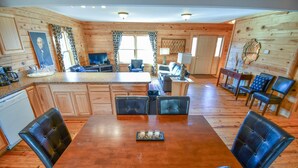 A wooden interior with a dining area featuring a wooden table and leather chairs, a kitchen with a refrigerator, and a living area with a sofa and a television. - Cabin 115, Luxury 6 bedroom, 3 bath cabin minutes from Downtown Lexington!  (Lexington)