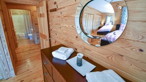 A wooden cabin interior with a bathroom visible through an open door, a round mirror on the wall, and neatly folded towels on the vanity. - Cabin 115, Luxury 6 bedroom, 3 bath cabin minutes from Downtown Lexington!  (Lexington)