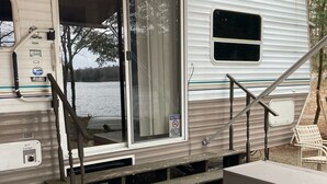 A recreational vehicle with a sliding door, a small outdoor seating area, and a kayak stored nearby.
