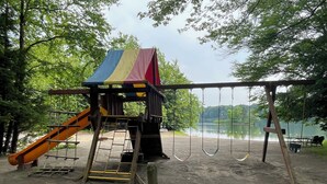 A playground with a slide, swings, and a climbing structure near a lake.