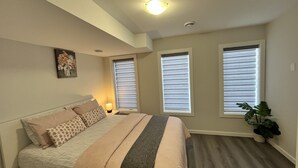 A bedroom with a bed, two windows with blinds, a ceiling light, and a potted plant. - Cozy Private 1-bedroom Basement Suite with free parking (Winnipeg)