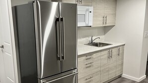 A modern kitchen with a stainless steel refrigerator, wooden cabinets, a microwave, and a sink. - Cozy Private 1-bedroom Basement Suite with free parking (Winnipeg)