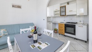 Uma cozinha moderna com armários brancos, forno embutido e um espaço de jantar com mesa posta para dois.