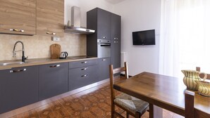 Cozinha moderna com armários cinza, bancada de madeira, forno embutido e televisão na parede.