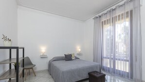 Quarto moderno com cama, mesas de cabeceira, uma cadeira e uma pequena mesa com uma planta.