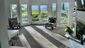 Une pièce spacieuse avec de grandes fenêtres, une cheminée et deux fauteuils à motifs.