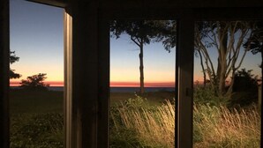 Une vue à travers une porte, donnant sur un paysage comprenant de l’herbe et des arbres, avec un coucher de soleil en arrière-plan.