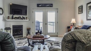 Un salon avec une cheminée, un téléviseur et une porte-fenêtre donnant sur un balcon.