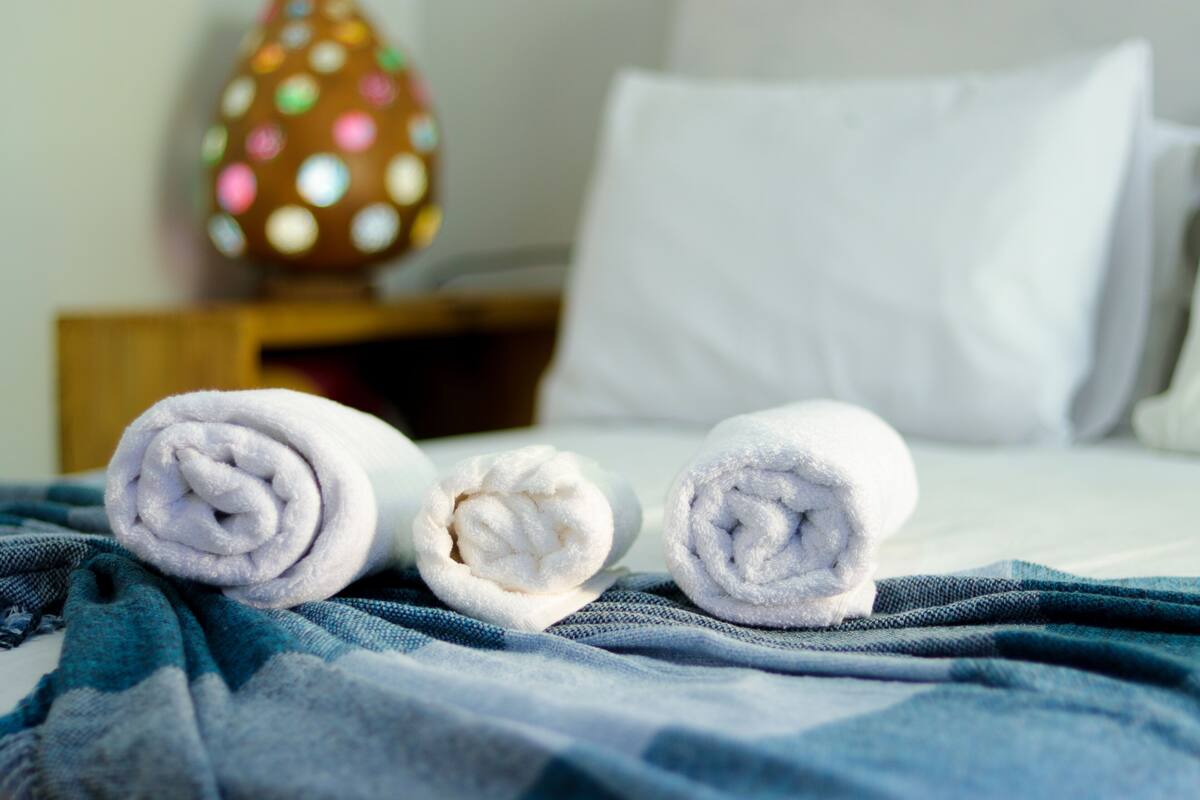 A neatly made bed with rolled white towels and a blue checkered blanket.