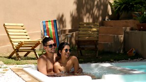 Una pareja en un jacuzzi con sillones de madera y una toalla a rayas al fondo.