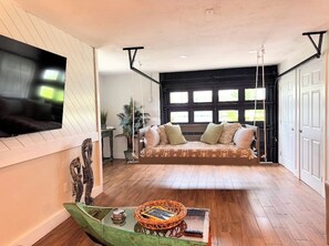 Een ruime woonkamer met een bank, een aan de muur bevestigde televisie en een houten vloer.