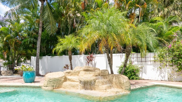 A swimming pool with clear water, surrounded by palm trees and a white wall. - Gulf Access Resort Style Pool Home Only 4 minutes to the Beach (Bonita Springs)