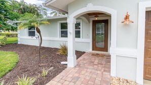 A house with a front porch, a palm tree, and a brick pathway leading to the entrance. - Gulf Access Resort Style Pool Home Only 4 minutes to the Beach (Bonita Springs)