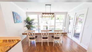 A dining area with a glass table and white chairs, large windows, and a wooden floor. - Gulf Access Resort Style Pool Home Only 4 minutes to the Beach (Bonita Springs)