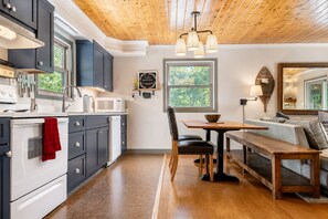A modern kitchen with dark cabinets, a white stove, and a red towel hanging on the oven. There is a dining area with a wooden table and chairs, and a bench.