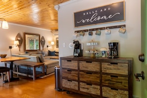 Un'accogliente zona giorno con soffitto in legno, un divano, un angolo caffè e un cartello di benvenuto.