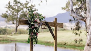 Un arco de madera decorado con flores, con un lago y árboles al fondo.