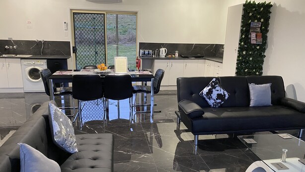 Una sala de estar moderna con un sofá negro, una mesa de comedor con sillas y una zona de cocina con una cafetera.