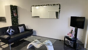 Una sala de estar moderna con un sofá negro, una mesa de centro de vidrio, un televisor de pantalla plana y un espejo decorativo.