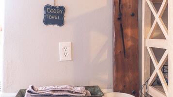 A wall-mounted sign reading "DOGGY TOWEL," a power outlet, a rustic wooden door, and a metal bucket with a towel.