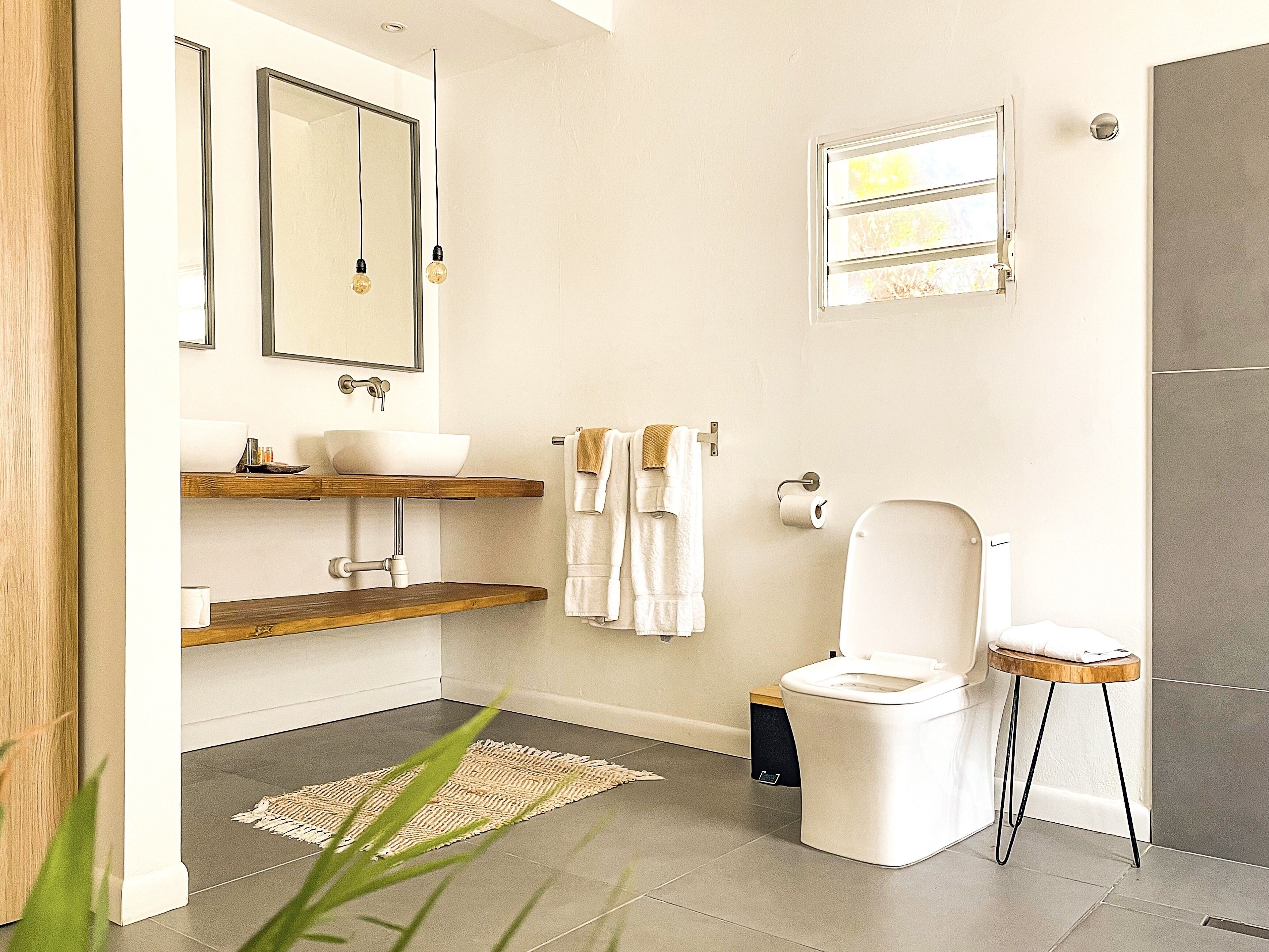 Un baño moderno con inodoro blanco, estantes de madera, un espejo grande y una ventana pequeña.