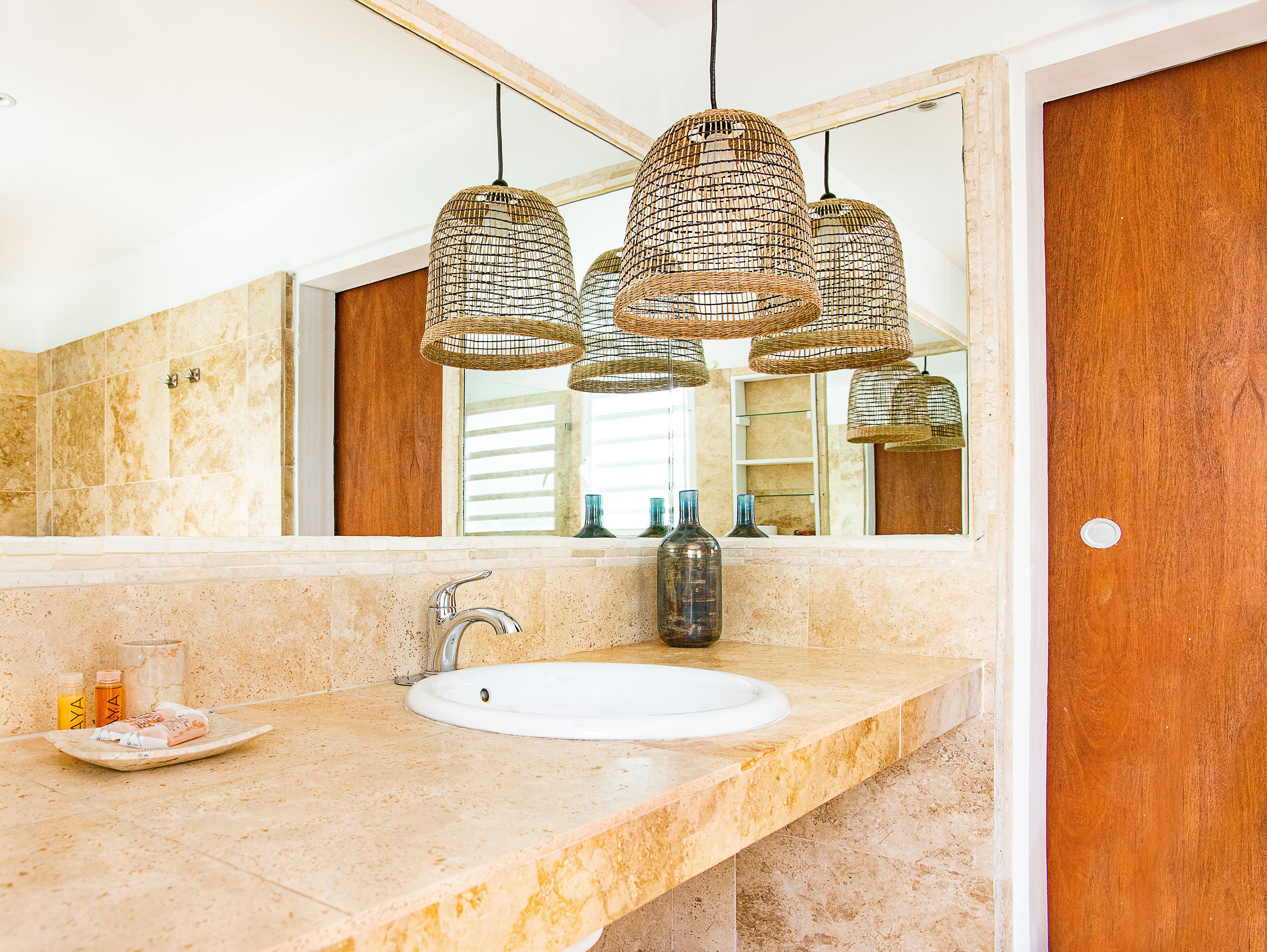 A bathroom with a white sink, a mirror, and three wicker pendant lights.