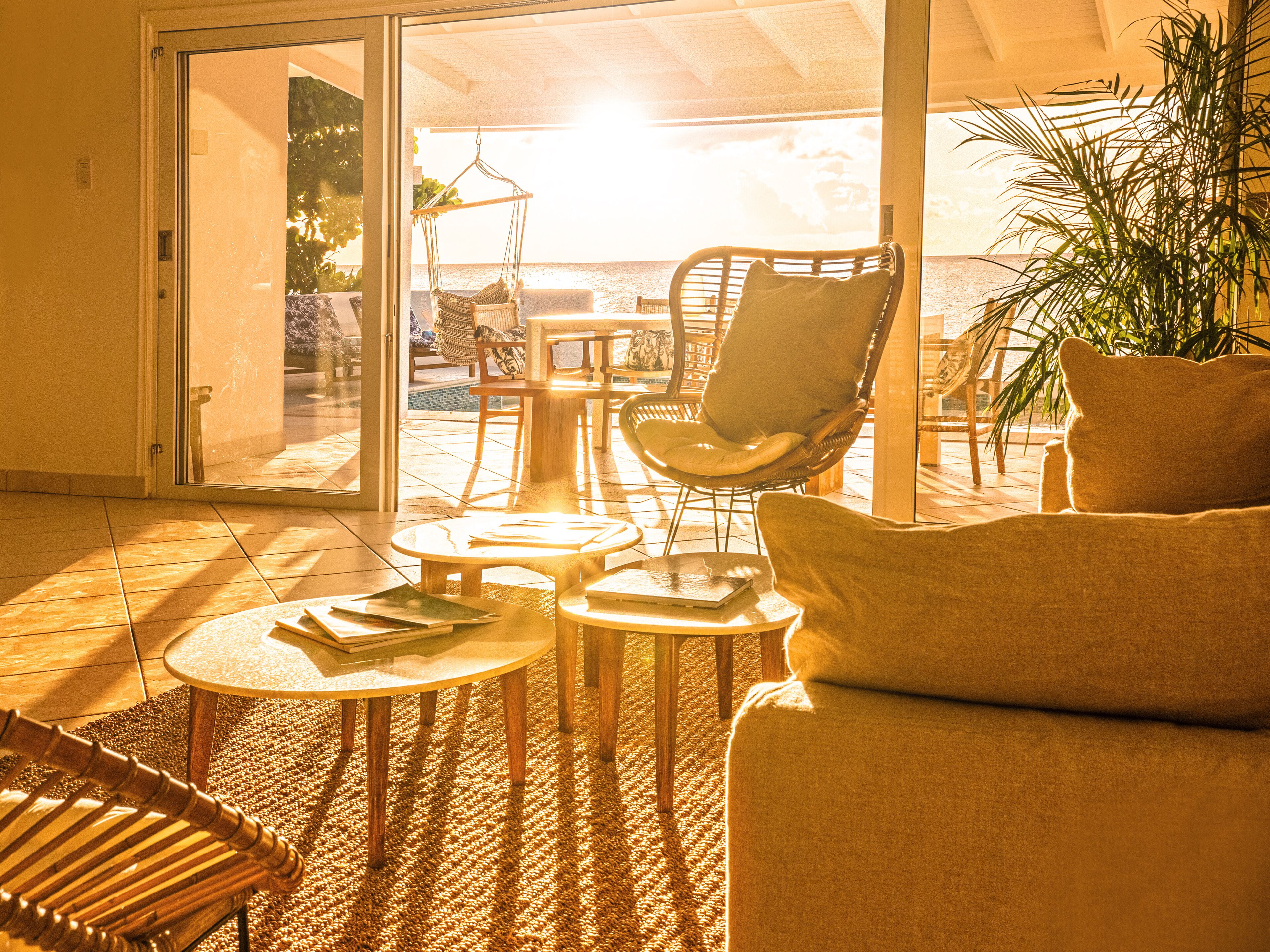 A sunlit room with a sliding glass door leading to a pool area, furnished with a sofa, chairs, and small tables.