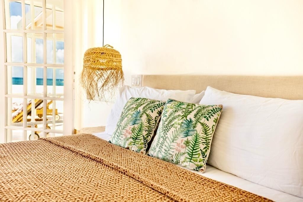 A bedroom with a bed, white pillows, a woven blanket, and a hanging light fixture.