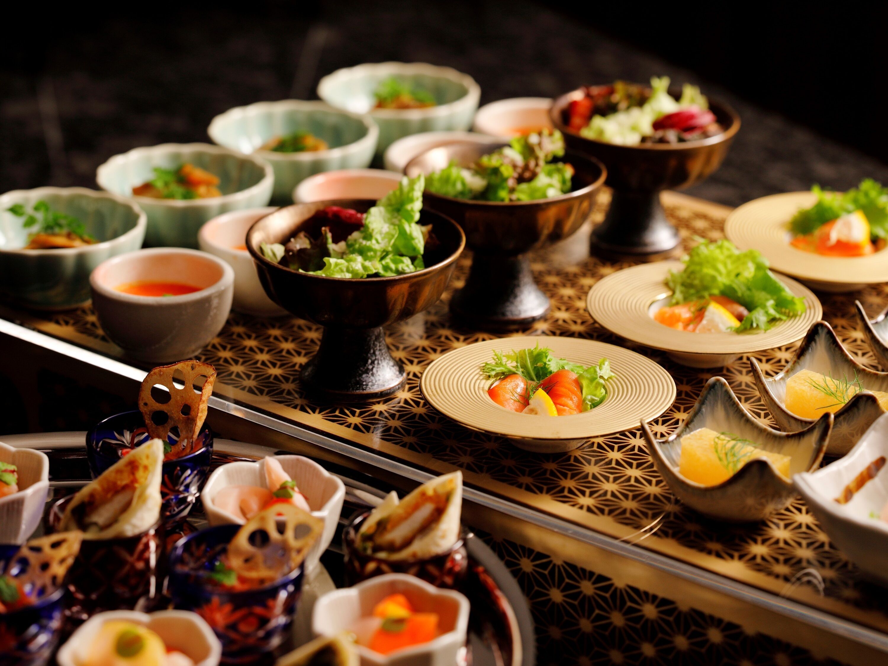 A table with various dishes, including sushi and salads, arranged on a patterned tablecloth.