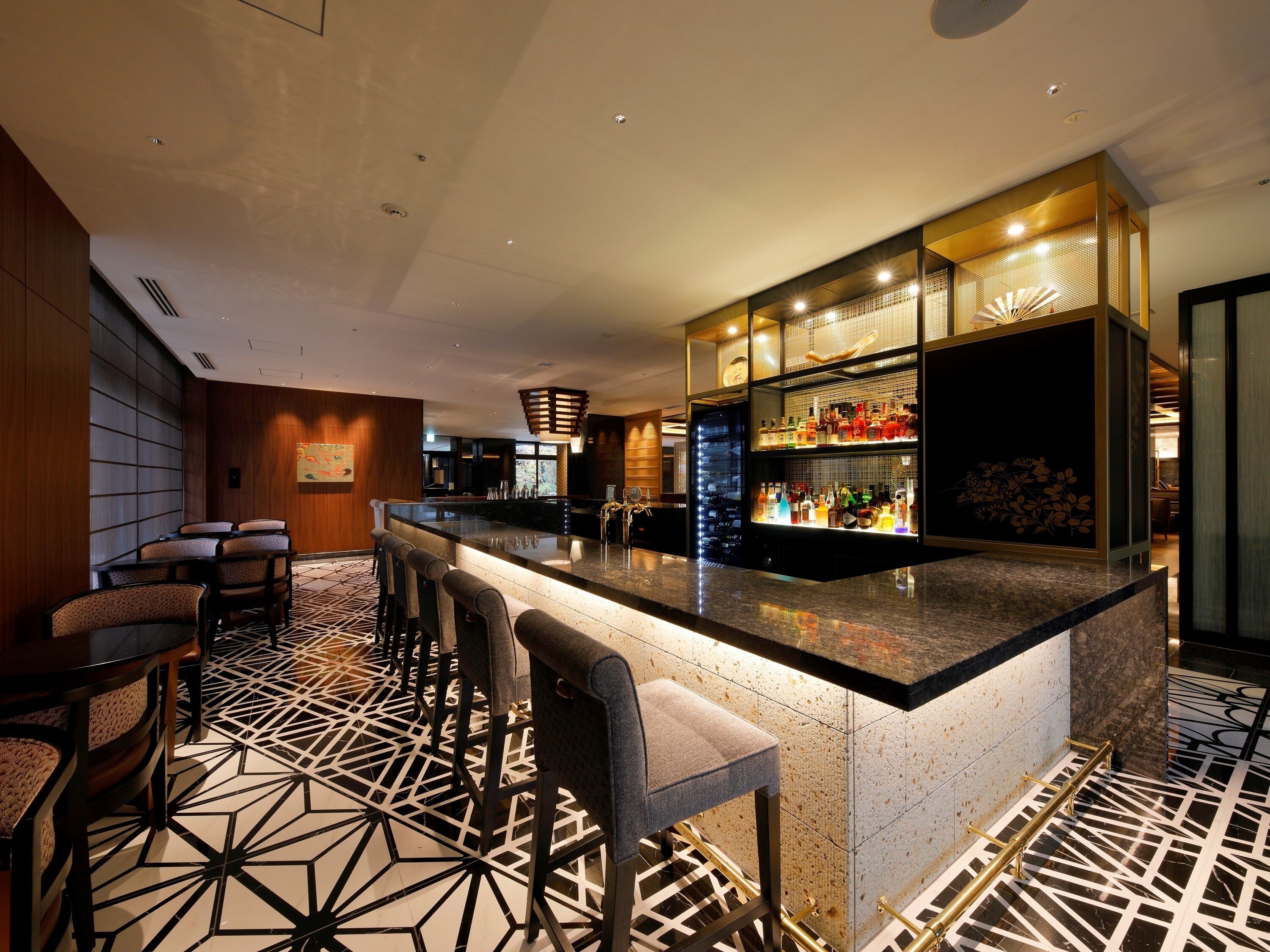 A modern bar area with a marble countertop, bar stools, and a display of liquor bottles.