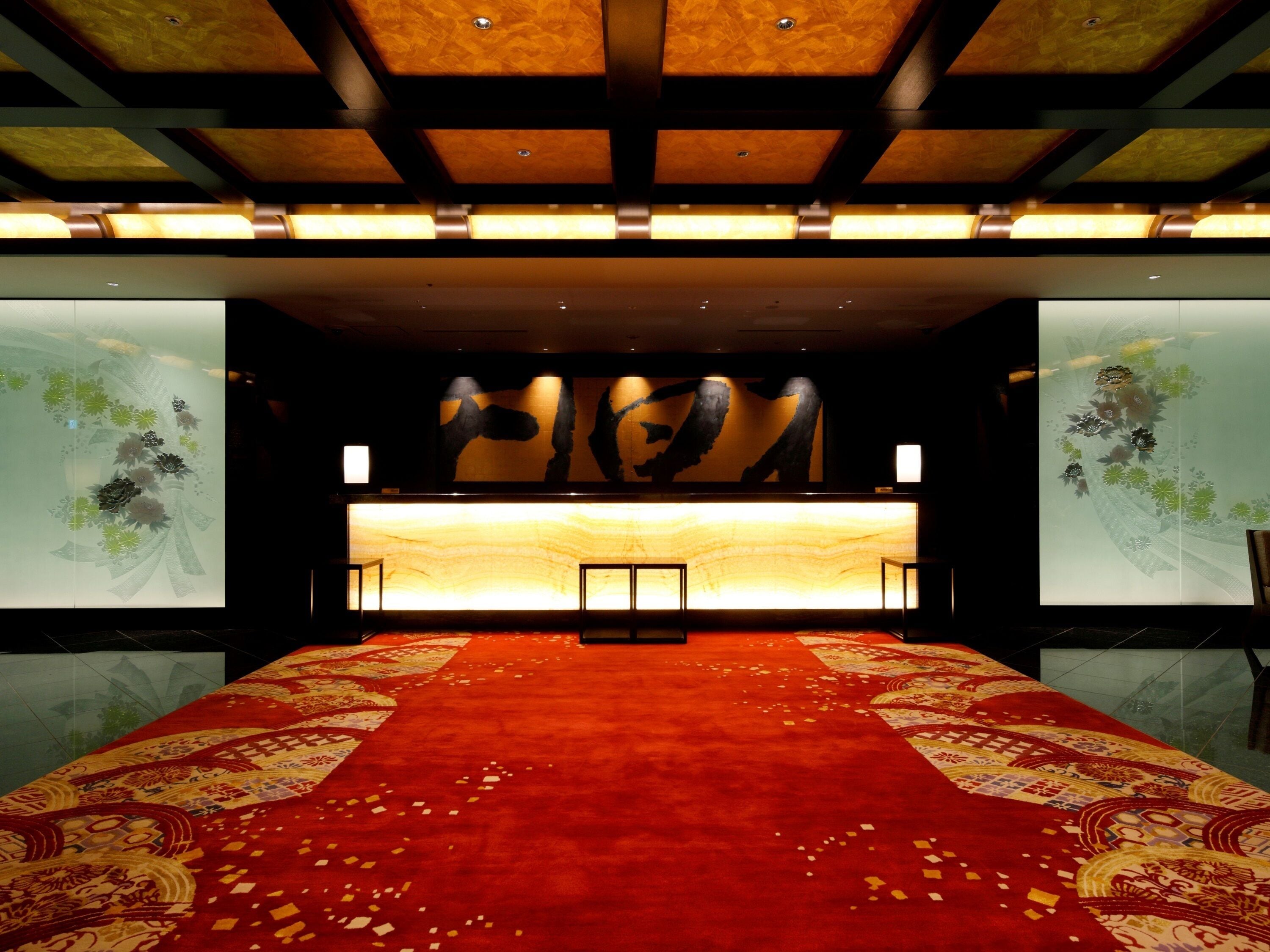 A hotel lobby with a red carpet, a reception desk, and large wall art.