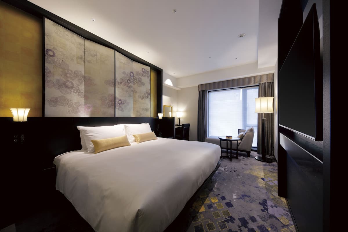 A hotel room with a large bed, a desk, a chair, and a TV.