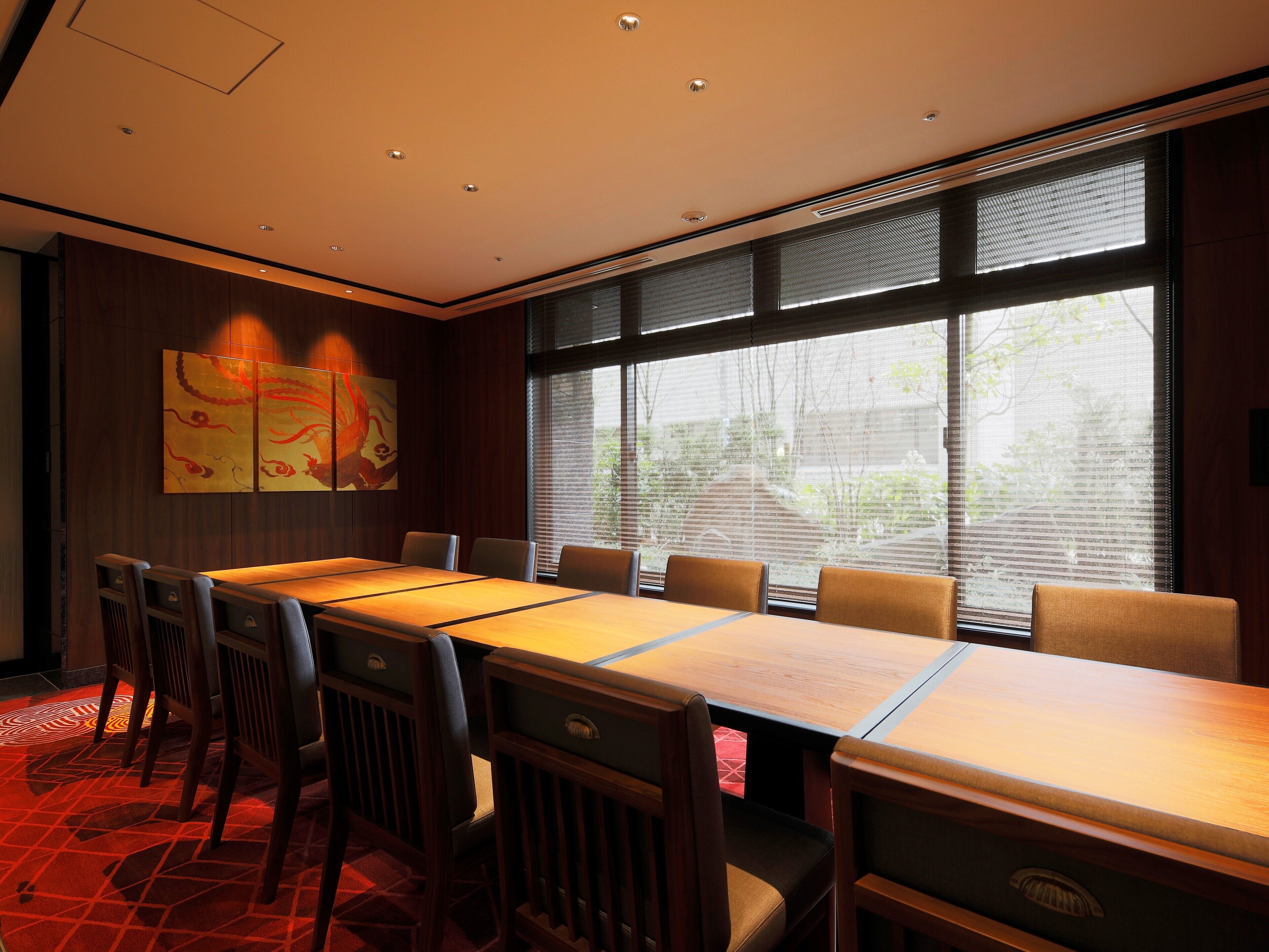 A conference room with a long table, chairs, and a large window with blinds.