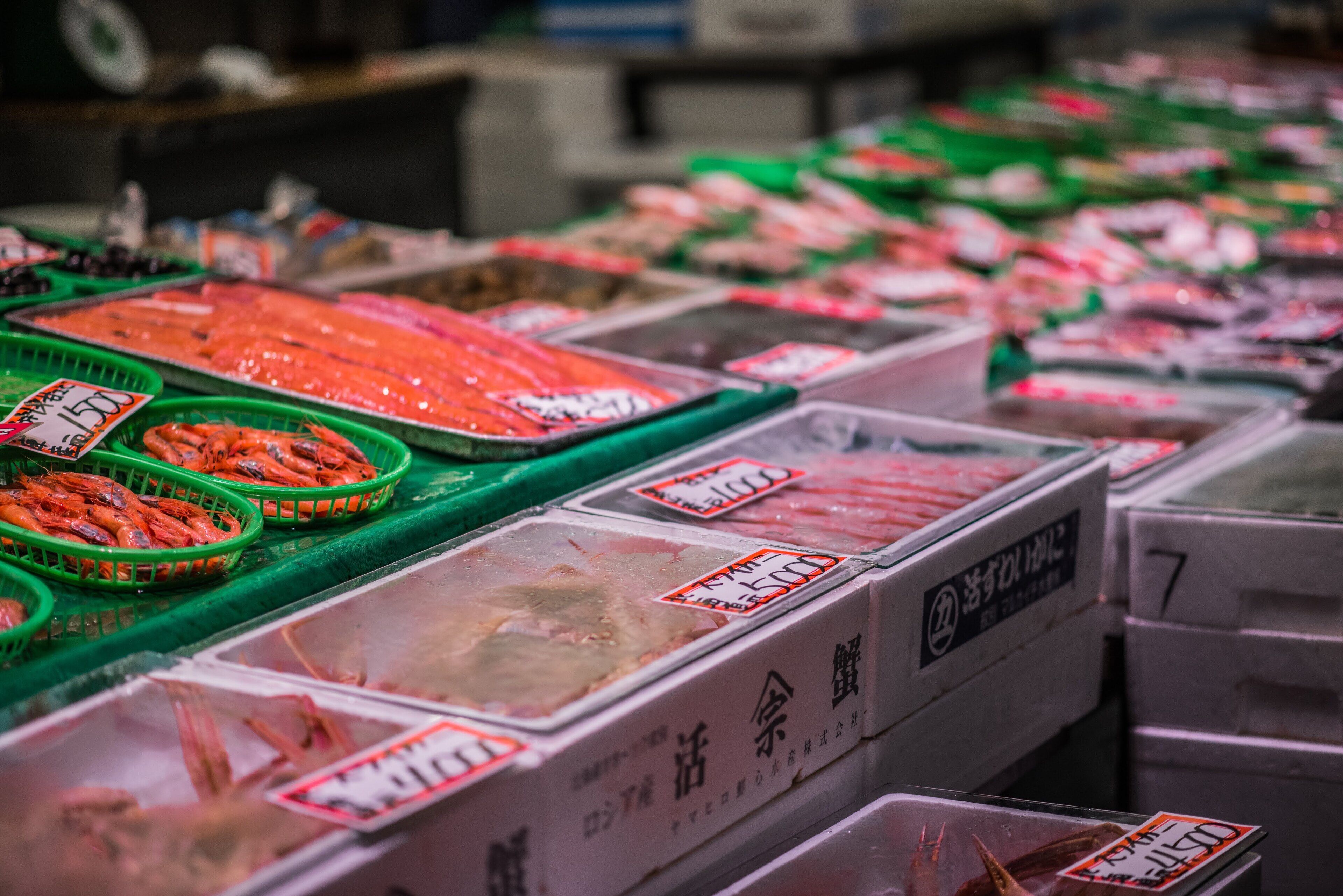 A seafood market with various containers of seafood, including shrimp and fish, displayed in green baskets and plastic containers.