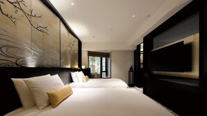 A modern hotel room with two large beds, a large flat-screen TV, and a view of trees through the window.