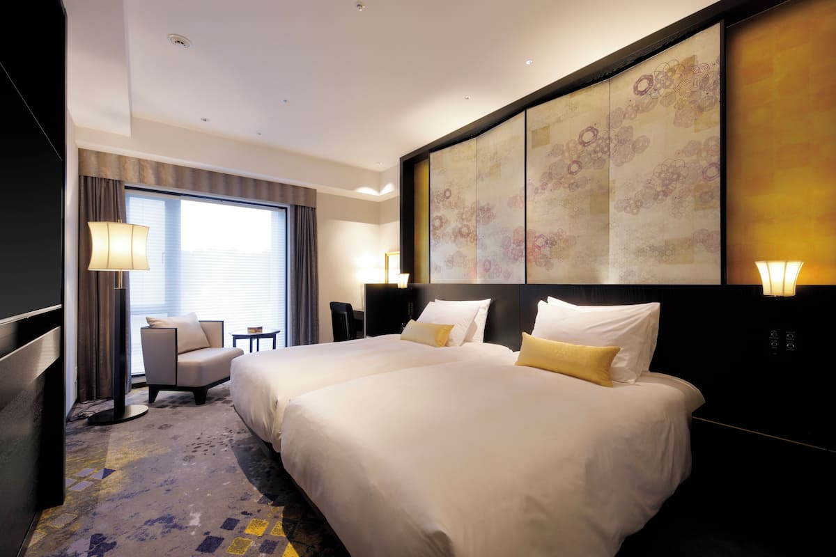 A hotel room with two beds, a desk, a chair, and a large decorative wall panel.