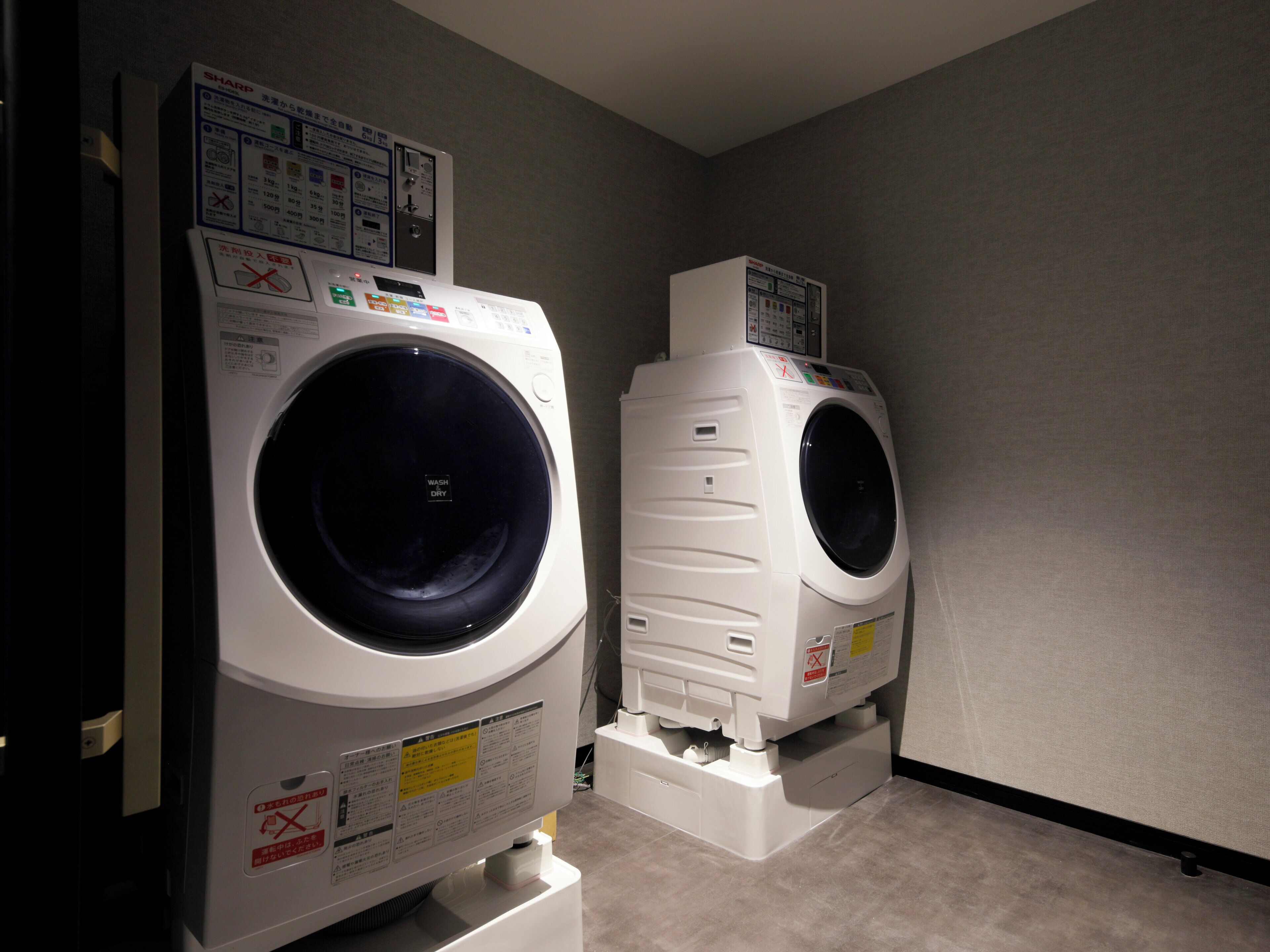 Two stacked front-loading washing machines in a laundry room with a grey wall and a white ceiling.