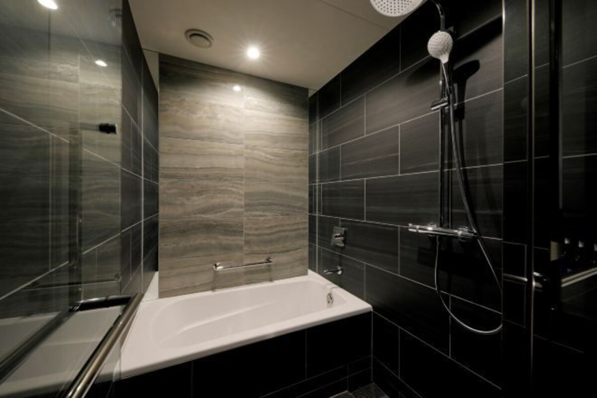 Un baño moderno con bañera, ducha con cabezal de ducha manual y zona de ducha con mampara de vidrio.