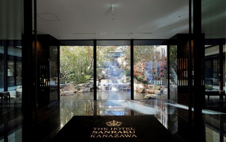 A hotel entrance with a glass door leading to a garden with a waterfall and rocks.