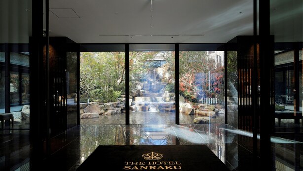 A hotel entrance with a glass door leading to a garden with a waterfall and rocks.