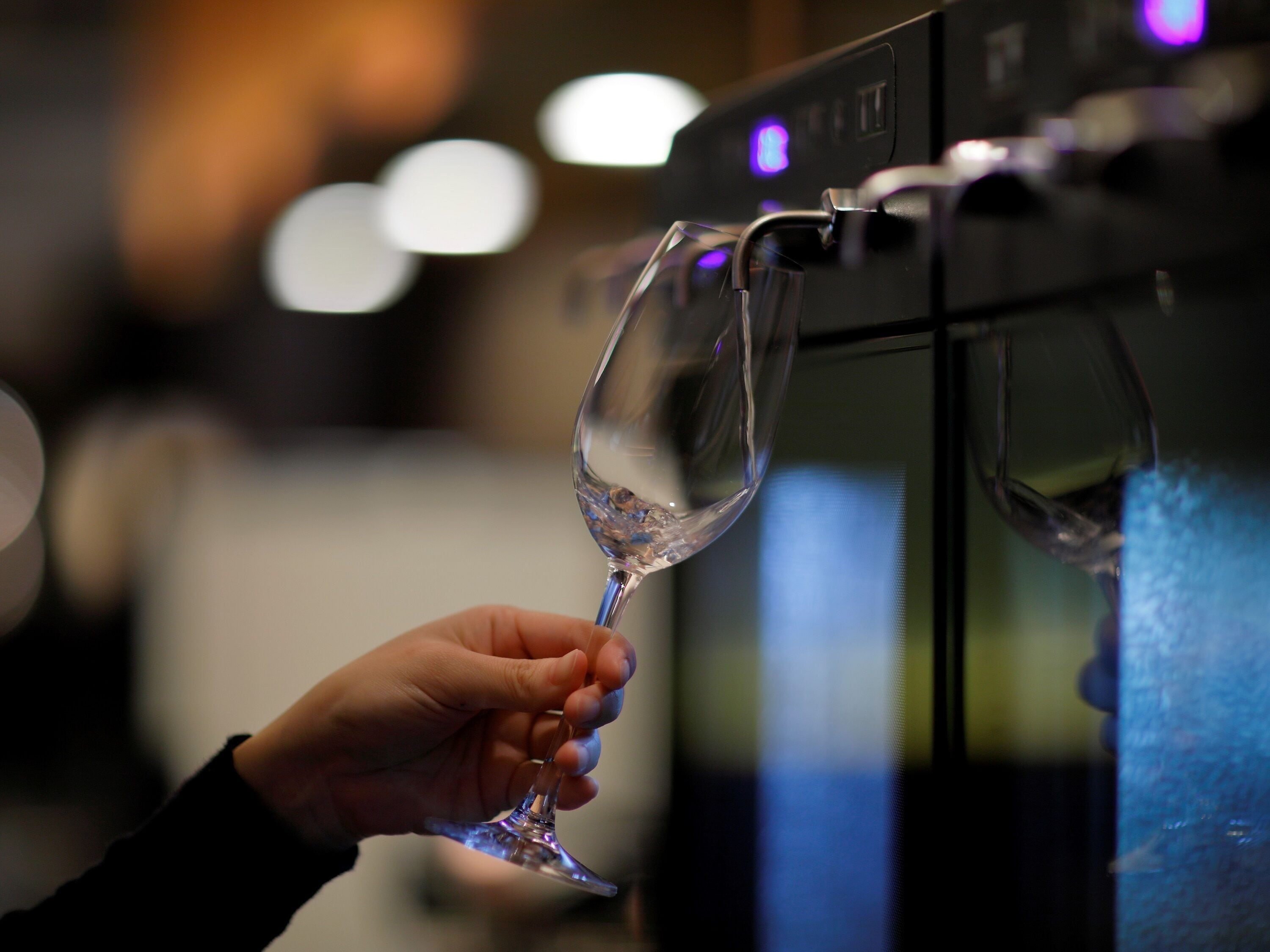 Une main tenant un verre à vin près d’un distributeur de vin.