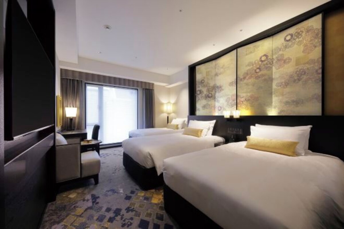 Habitación de hotel con dos camas, un escritorio, una silla y una obra de arte floral grande en la pared.